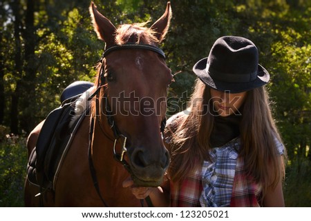 Young cowgirl in hat with bay horse