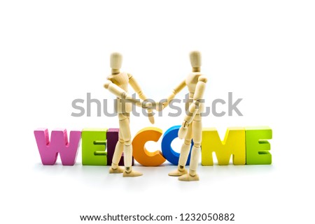 Wooden figures posing as business men shaking hands in front of the word WELCOME, high key isolated on white.