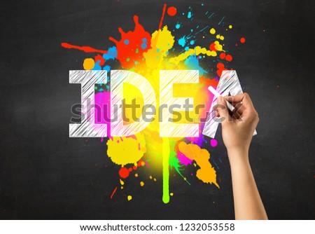 Female hand holding white chalk in front of a blackboard with idea written on it and a colorful splash in the background