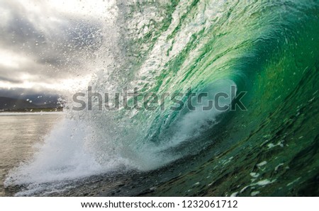 A hollow wave crashes as sun refracts through the emerald ocean water on a sunny day.  The waves are perfect for surfing.