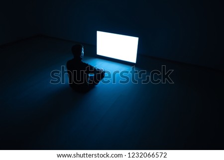 The man sitting in the dark room in front of a white screen