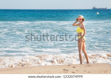 Happy smiling young woman in sun hat walking on beach along seaside, summer sea vacation and travel concept