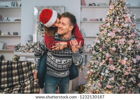 Tender and touching picture of young woman kissing man. She sits on his back and embraces. They spend time together in decorated room.