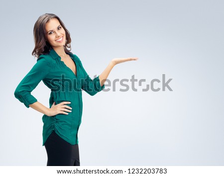 Portrait of beautiful woman in green confident clothing showing something or empty copyspace place for some slogan, text message, or product, against grey background. Business and advertising concept.
