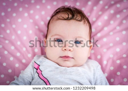 Closeup image of the face of the deep blue eyes baby girl looking at the camera portrait. Happy childhood concept image. Smart and serious newborn baby portrait.