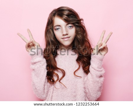 happy people concept - smiling little curly girl showing peace gesture with fingers