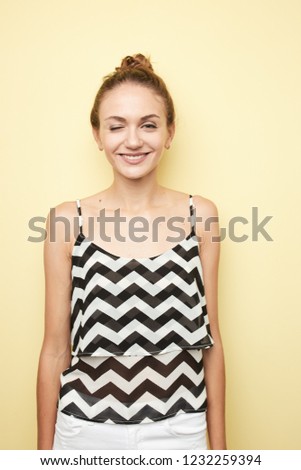 Cheerful girl  dressed in a striped top winks in the studio  on the yellow background