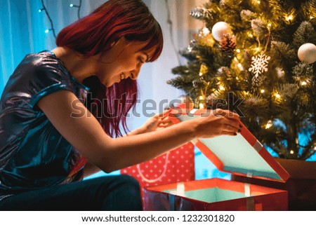 Cheerful woman opening Christmas gift box under tree at home