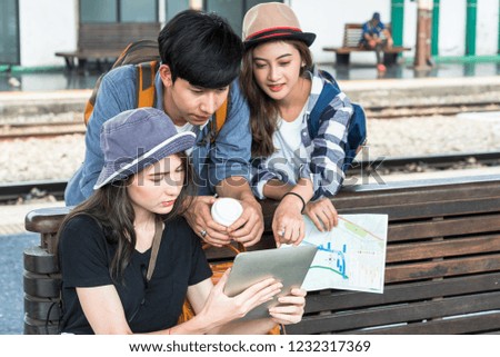 Young asian traveling  group holding a paper map and tablet planing travel trip for holiday destination. Photography in public place at Bangkok railway station.