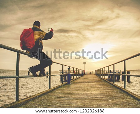 Man tourist taking a photo on cellphone of the ocean.   Traveler standing on pier and taking photo of the bridge at the bay