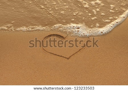 Heart drawing in the sand and wave on the morning beach