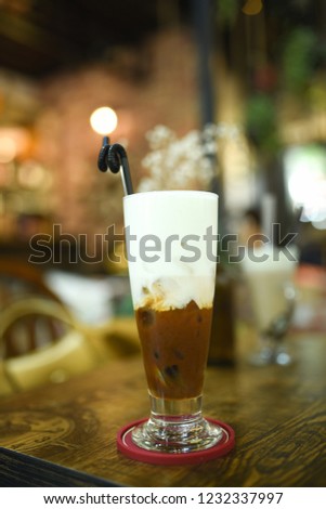 A glass of ice coconut coffee  at coffee shop on a wooden table. A cup of layer coffee and milk blurry background by  a vintage shop. Testy mocha coffee with milk.