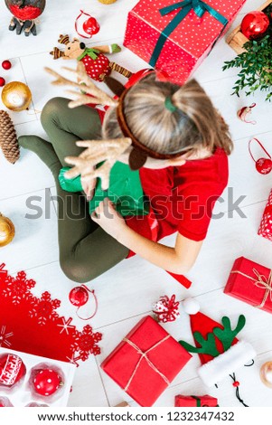 Cute girl sitting on the floor opening christmas present, top view.