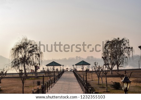 Amazing sunset view of Dal lake from Mughal garden, Srinagar. Dry winter landscape with a pavement covered with dry trees with hut structure at distance and dal lake in the backdrop in Kashmir, India.