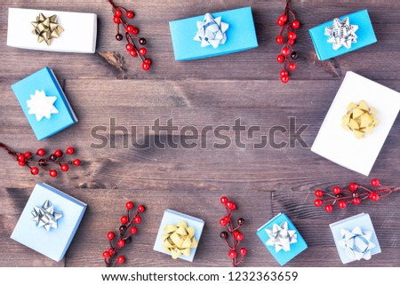 Small white and blue boxes with golden bows, twigs with red berries. Christmas composition with copy space. Festive layout with place for text, on a dark wooden background.