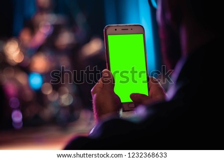 Man's hand shows mobile smartphone with green screen in position isolated on green background