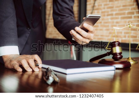 Justice and law concept. Gavel on sounding block in hand's Male judge at a courtroom, working with smart phone, report the case on table in modern office.
