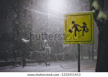 Caution! School zone crossing road sign covered with snow in winter at the evening,