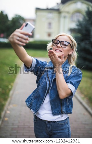 Beautiful tourist woman hand holding smart phone photo camera lens, taking selfies pictures on holiday destination, blowing kisses, smiling looking outdoors. Travel technology recreation lifestyle.