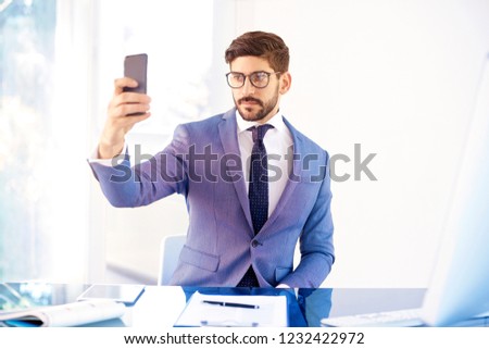 Portrait shot of young businessman using his mobile phone and taking self portrait while working in the office. 
