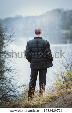 A man in a warm black jacket retired on the river bank