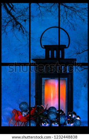 Lantern with a candle behind a window with a tree silhouette and dark night sky. 
