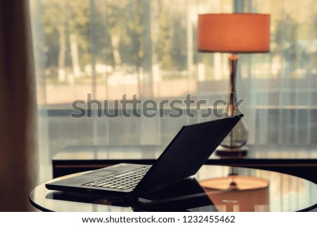 Laptop stands on a glass table near a window with a yellow lamp