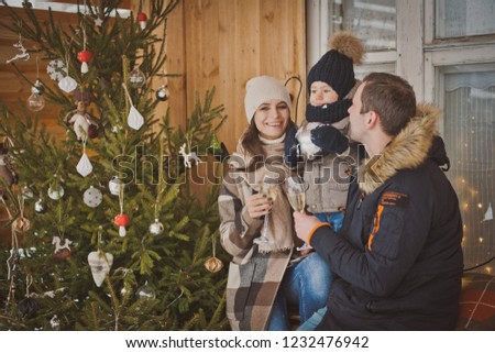 Russian young family enjoying their holiday time together, decorating Christmas tree outdoors in warm clothes, arranging the christmas lights and having fun. mother father and son meet new year