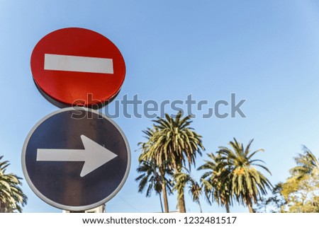 Forbidden road sign and direction sign, with palm trees in the background, on a sunny day