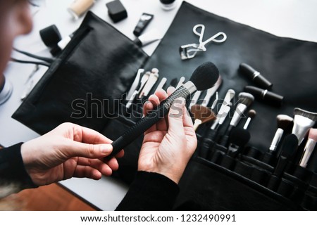 Make up artist preparing for photo shoot. A lot of make up brushes with metal details placed on the table in brush roll.  Accessories on grey background.