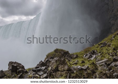Green rocky foreground in front of waterfall with overcast sky