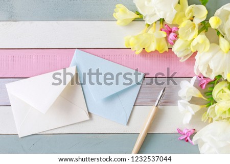 Beautiful freesias and tulips on striped wooden background. Envelopes and vintage pen among spring flowers. 