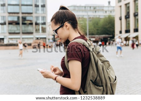 A tourist girl with a backpack or a student on a square in Leipzig in Germany uses a mobile phone to view a map or call or for another.