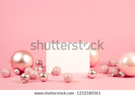 Mock up with invitation card on trendy pastel light pink background with christmas ornaments. Greeting card and pink Christmas baubles