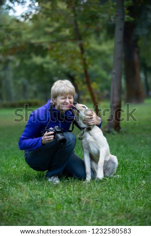 Professional photographer. Portrait of confident adult woman holding camera in hands and taking photo of the  dog  in the park 