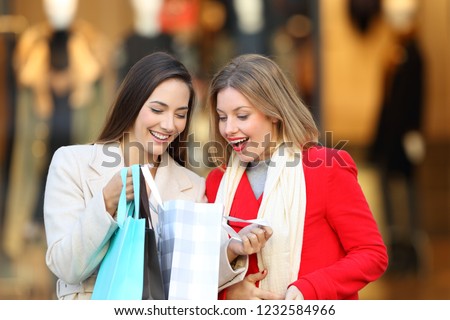 Front view of two happy shoppers checking purchases in a shooping bag in a commercial centre