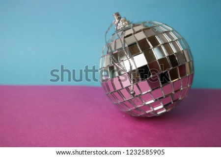 Silver mirror musical club disco ball small round glass winter shiny decorative beautiful xmas festive Christmas ball, Christmas toy plastered on glitter on a gray pink purple background.