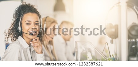 Call center worker accompanied by her team. Smiling customer support operator at work. Young employee working with a headset. Royalty-Free Stock Photo #1232587621