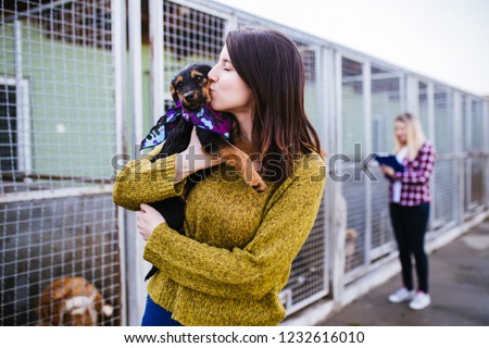 Young woman with worker choosing which dog to adopt from a shelter. Royalty-Free Stock Photo #1232616010