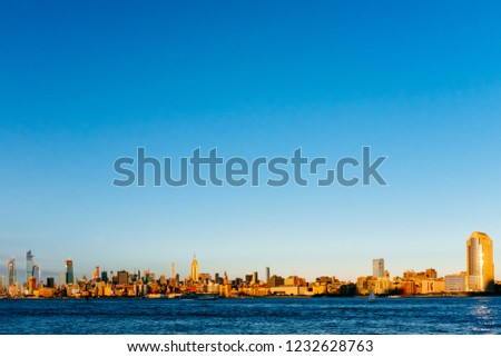 View of the skyline of midtown Manhattan over Hudson River under blue sky, at sunset, with Empire Sate Building, viewed from New Jersey, in New York City, USA