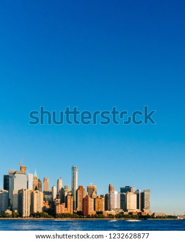 View of the skyline of downtown Manhattan over Hudson River under blue sky, at sunset, viewed from New Jersey, in New York City, USA