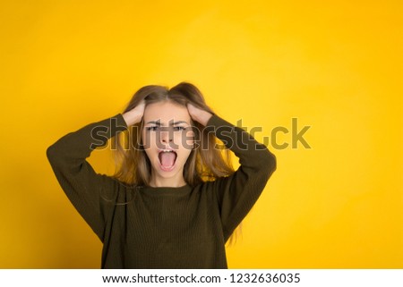 Portrait of an angry young woman dressed in sweater standing isolated over yellow background, screaming hard