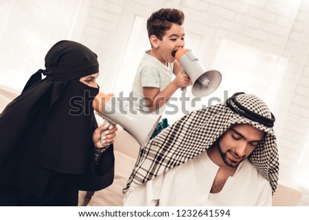 Wife and Son with Loudspeakers Screaming to Father. Woman in Black Veil. Parent with Child Indoor. Upset Family. Man with Laptop. Young Arabian Woman. Muslim Family. Using Digital Device at Home.