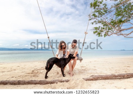 Young couple swinging on a swing on paradise tropical beach with dog, honeymoon, vacation, travel concept