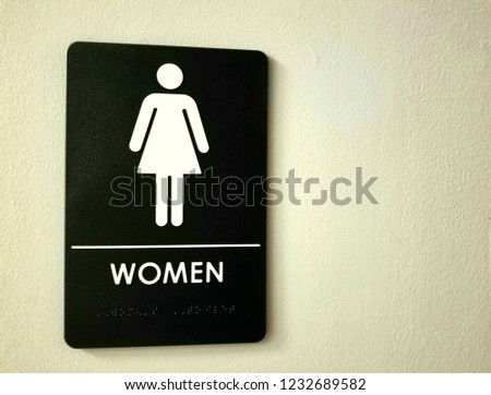 A stick-figure icon of a woman, generally used to indicate a female restroom, with the word WOMEN in English and Braille

