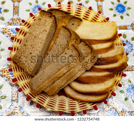Sliced pieces of rye and white bread on a wicker plate on a background of colored tablecloth closeup