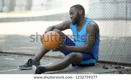 Lonely black basketball player sitting on stadium ground and holding ball, sport