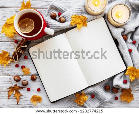 autumn flatlay on wooden backdrop with a notebook, cup of tea and fallen dry yellow leaves