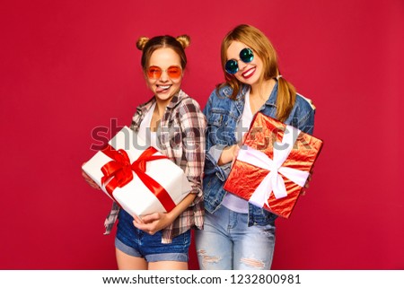 Christmas, x-mas, concept.Two smiling beautiful women in stylish clothes.Girls posing on red background.Models with big gift boxes.Having fun,ready for celebration.Bright holiday of best friends