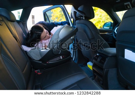 Mother kissing her baby in baby seat on the backseat of the car with black interior, viewed from other side of the vehicle with copy space